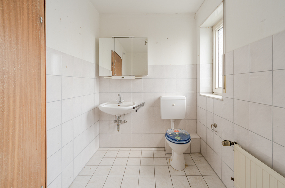 Helles Bad mit Waschbecken, Spiegel, Toilette und Fenster, gefliest an Wänden und Boden.