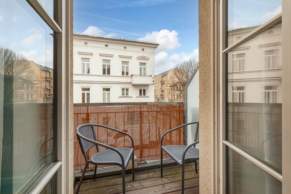 Kleiner Balkon mit zwei Stühlen, Blick auf Nachbargebäude und blauen Himmel.