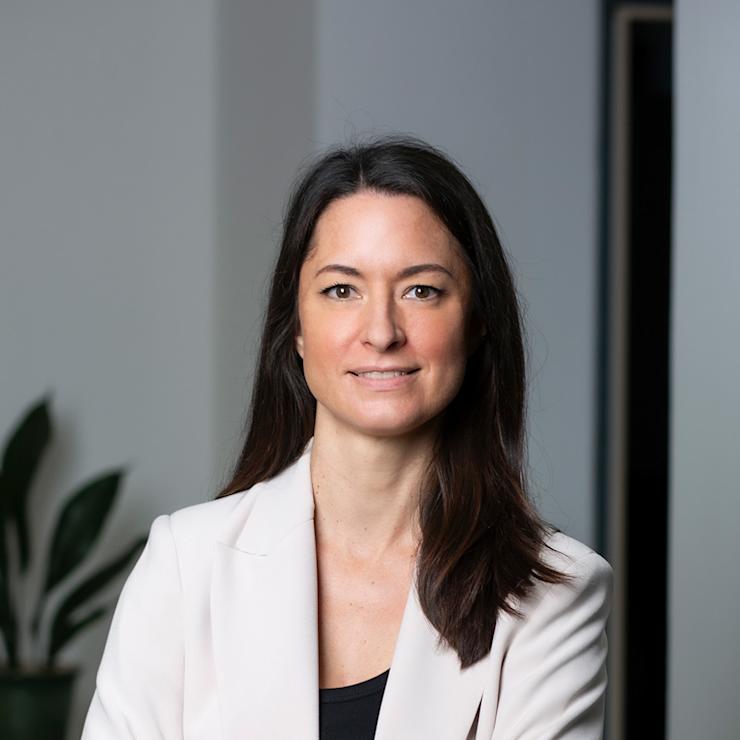 Frau mit langen dunklen Haaren steht mit verschränkten Armen in einem modernen Raum.