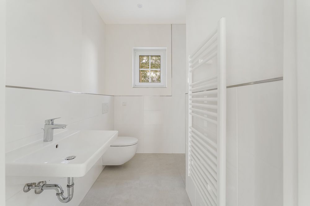 Helles, modernes Badezimmer mit Waschbecken, Toilette, Handtuchheizkörper und Fenster.