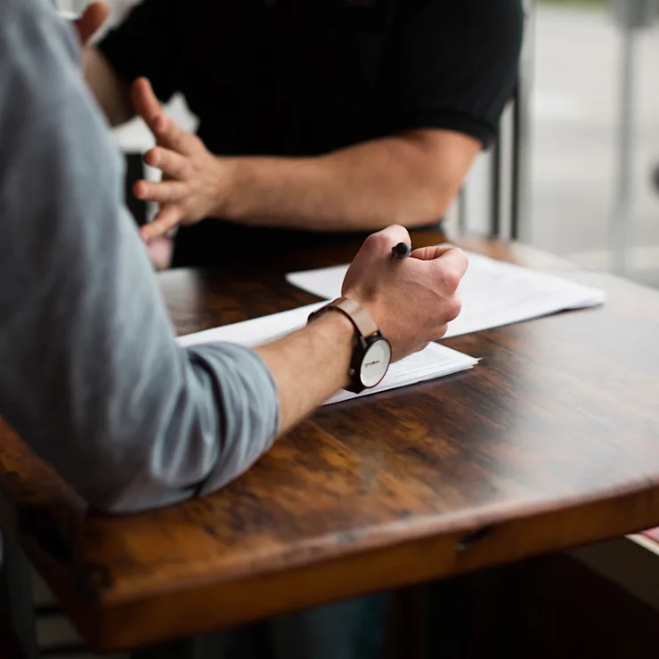 Zwei Personen sitzen an einem Holztisch und besprechen Dokumente.