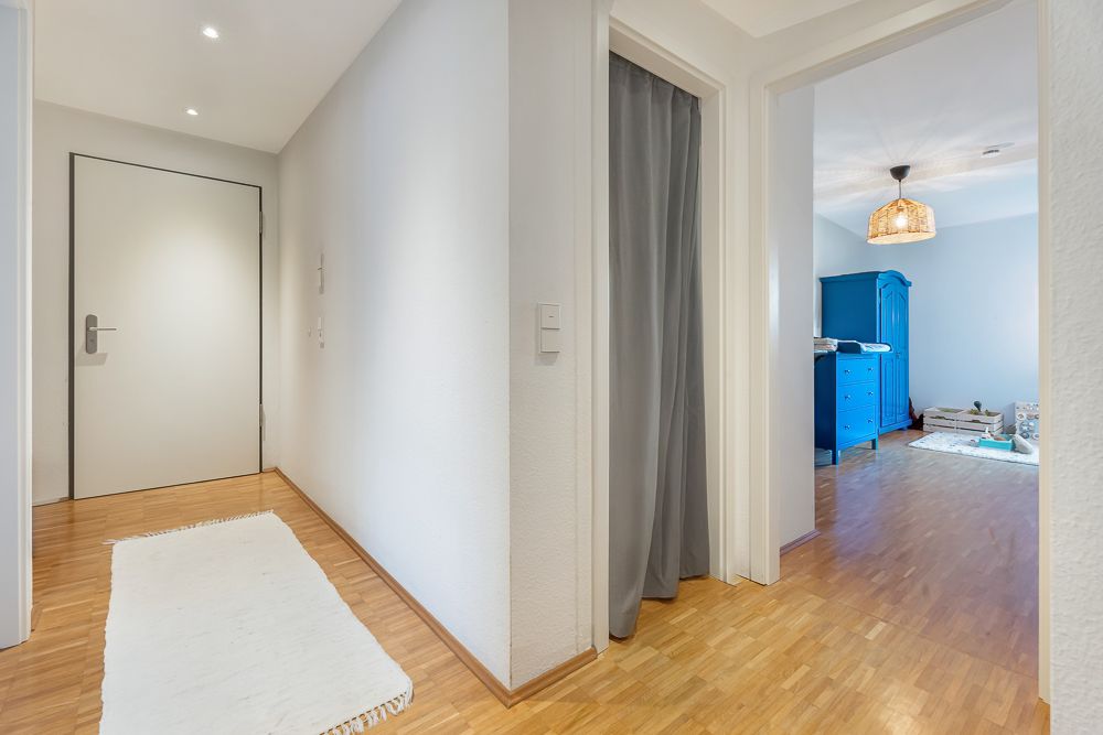 Heller Flur mit Holzboden, weißem Teppich und Zugang zu einem Zimmer mit blauem Schrank.