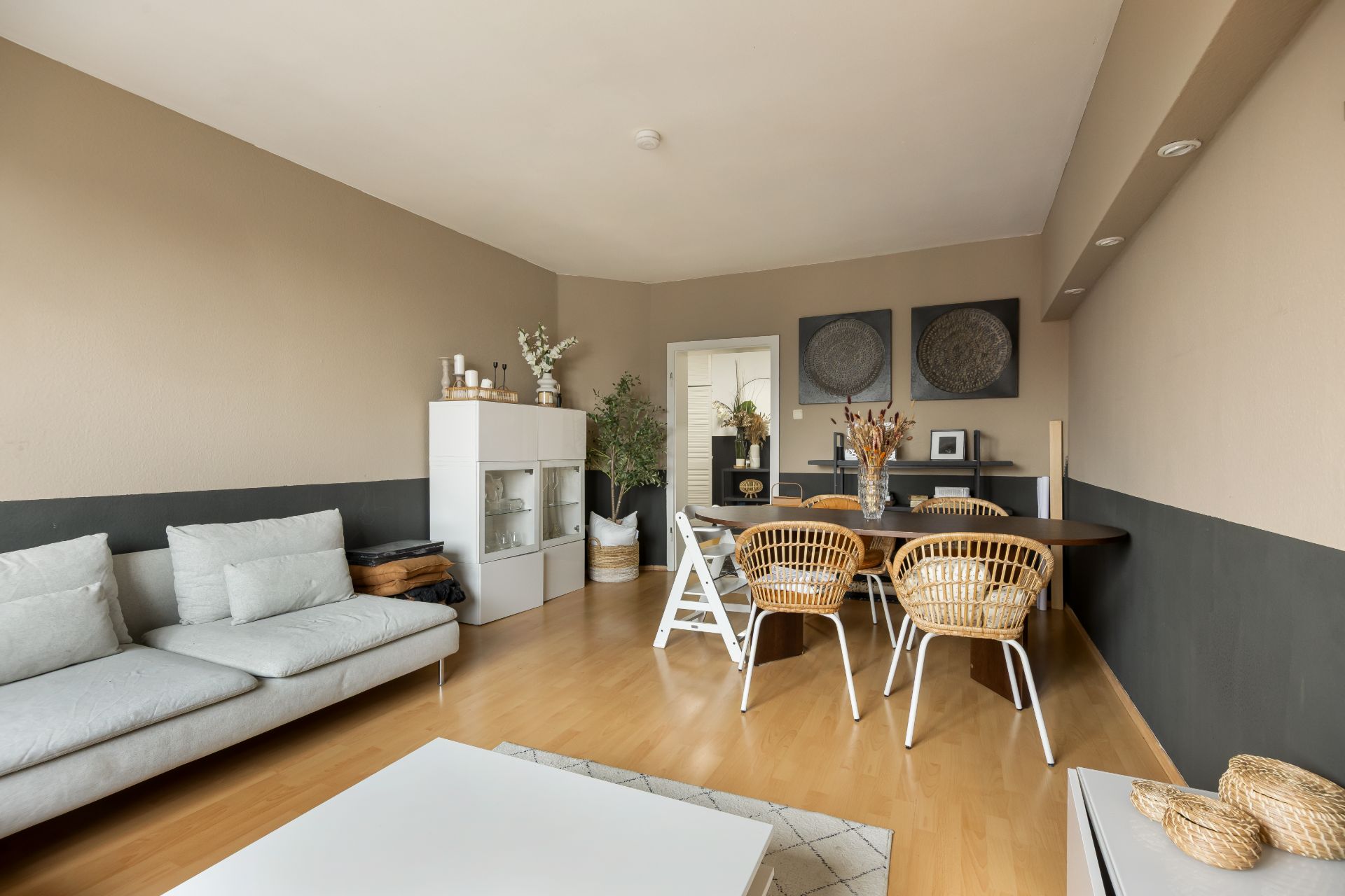 Helles Wohnzimmer mit Sofa, Essbereich, Holzboden und Dekorationen.