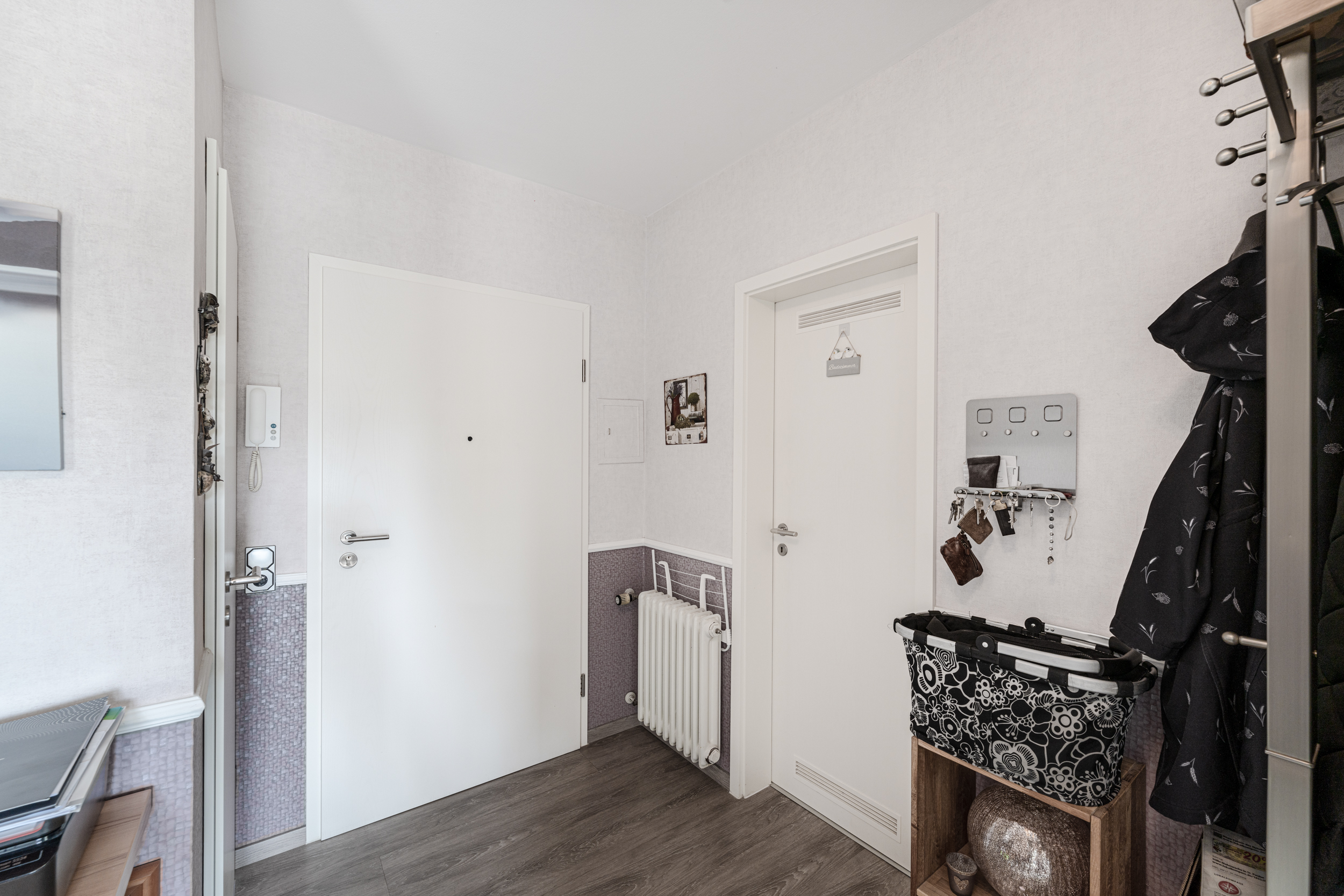 Heller Flur mit zwei weißen Türen, Garderobe, Schlüsselbrett und Holzregal.