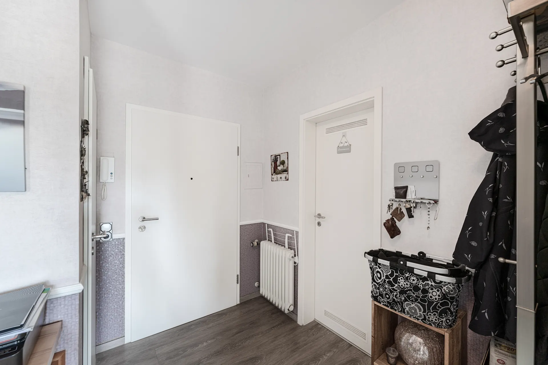 Heller Flur mit zwei weißen Türen, Garderobe, Schlüsselbrett und Holzregal.
