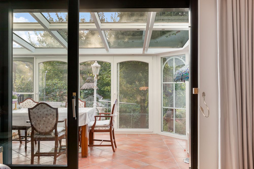 Wintergarten mit Glasdach, Esstisch und Stühlen, Blick nach draußen in den Garten.