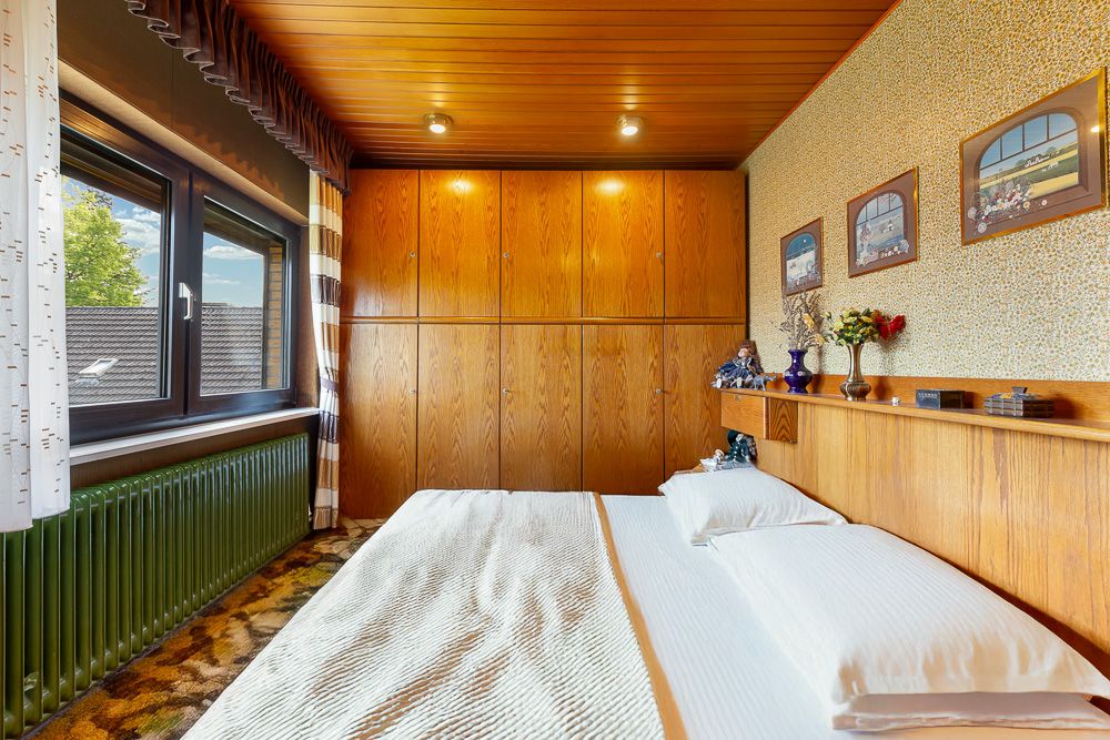 Schlafzimmer mit Doppelbett, Holzwand, großem Fenster und Dekorationen auf einem Regal.