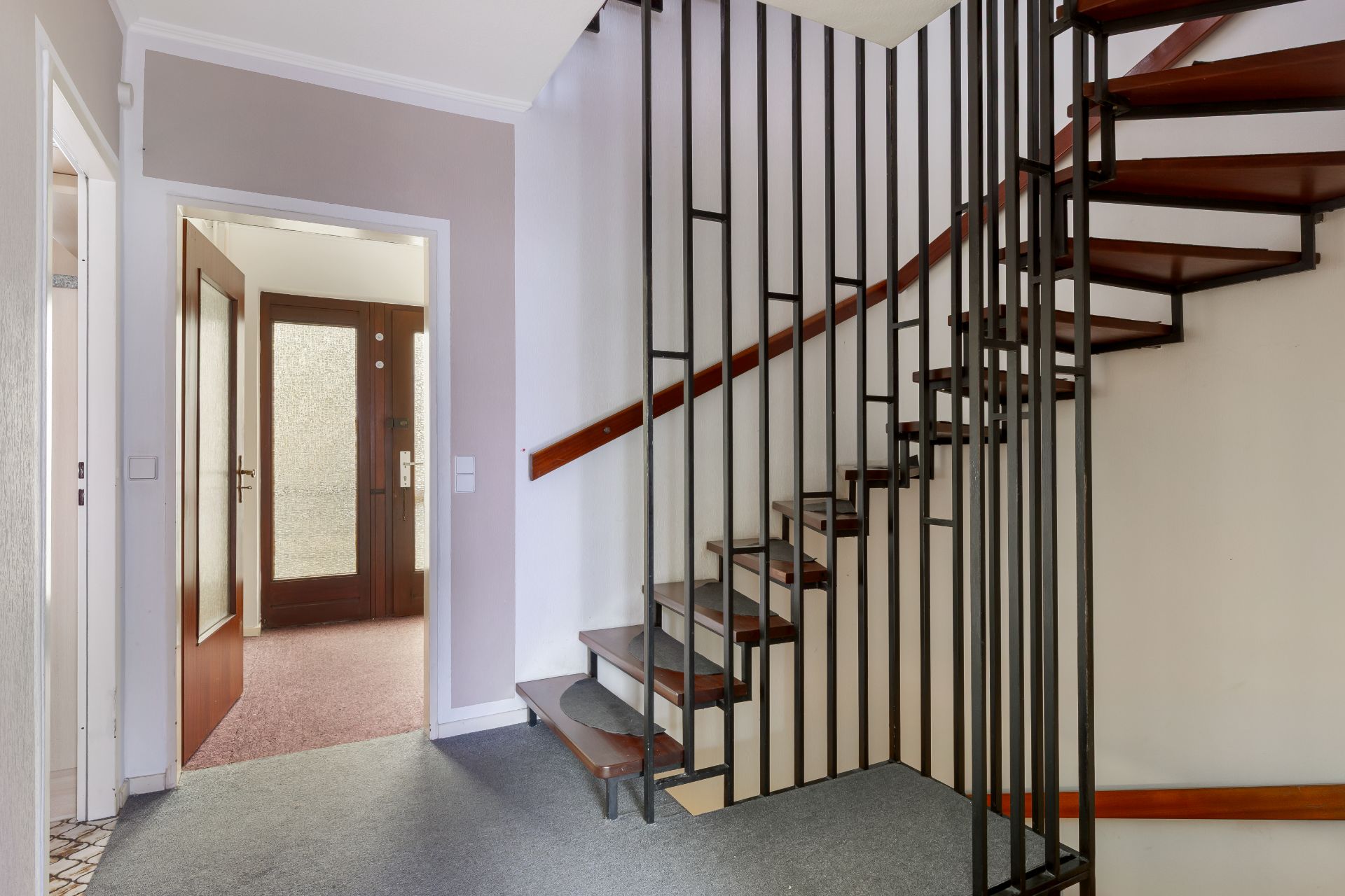 Eingangsbereich mit offener Holztreppe und schwarzem Geländer, Tür zur Diele offen.
