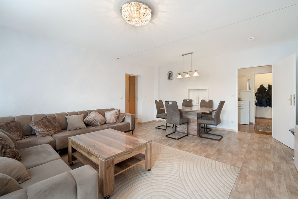 Helles Wohnzimmer mit großer Eckcouch, Holztisch, Esstisch und sechs Stühlen auf Holzfußboden.