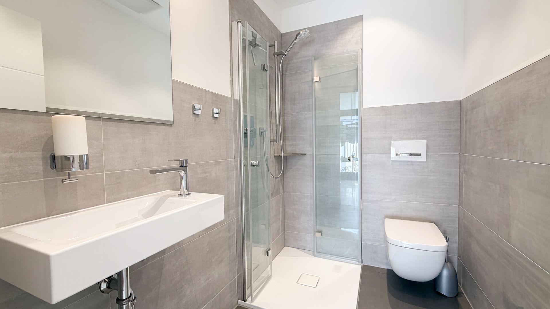 Modernes Badezimmer mit Waschbecken, Dusche und wandhängendem WC, alles in grauen und weißen Tönen.