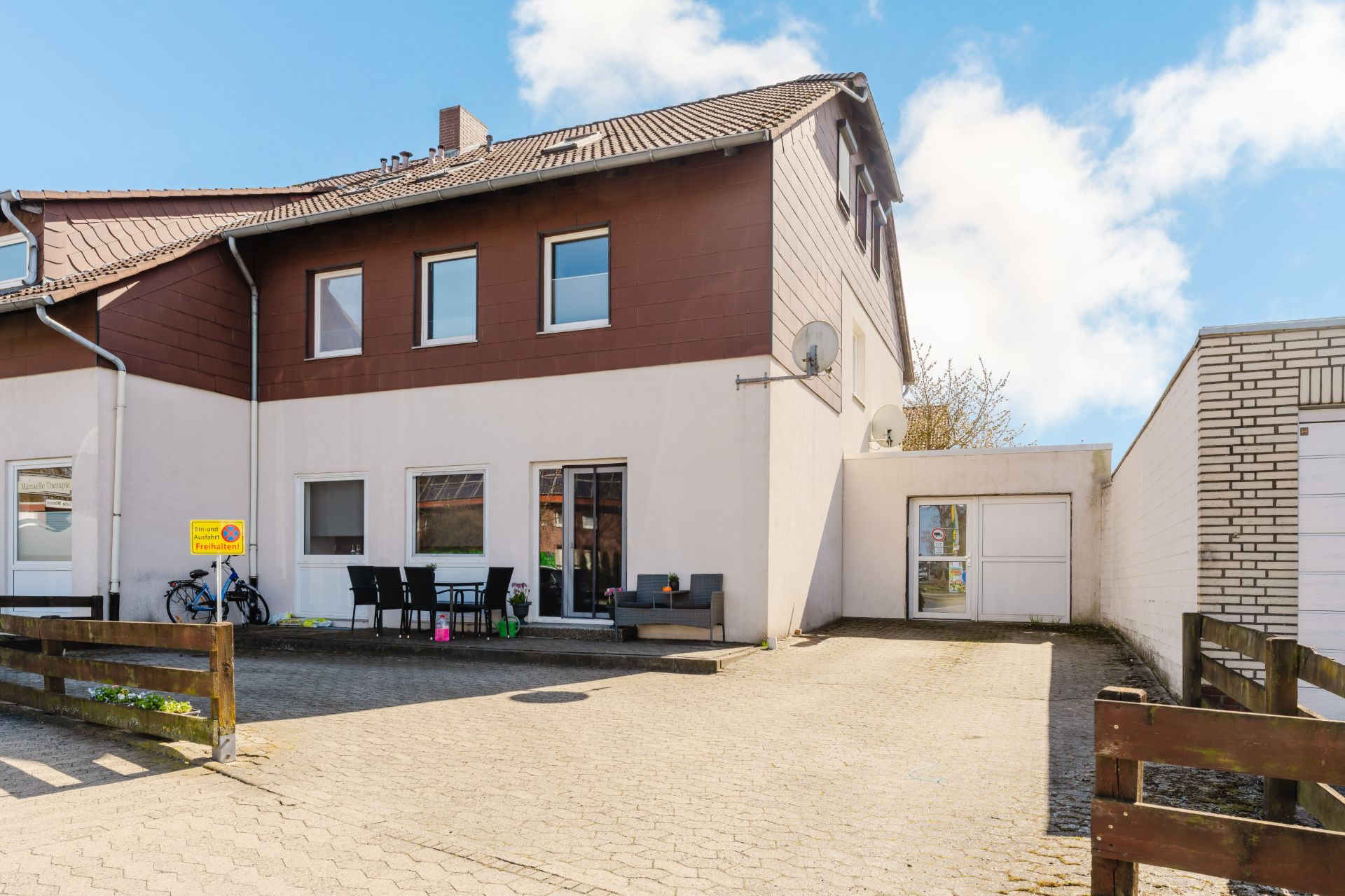 Zweistöckiges Wohnhaus mit Terrasse, Gartenmöbeln und gepflastertem Hof vor dem Haus.