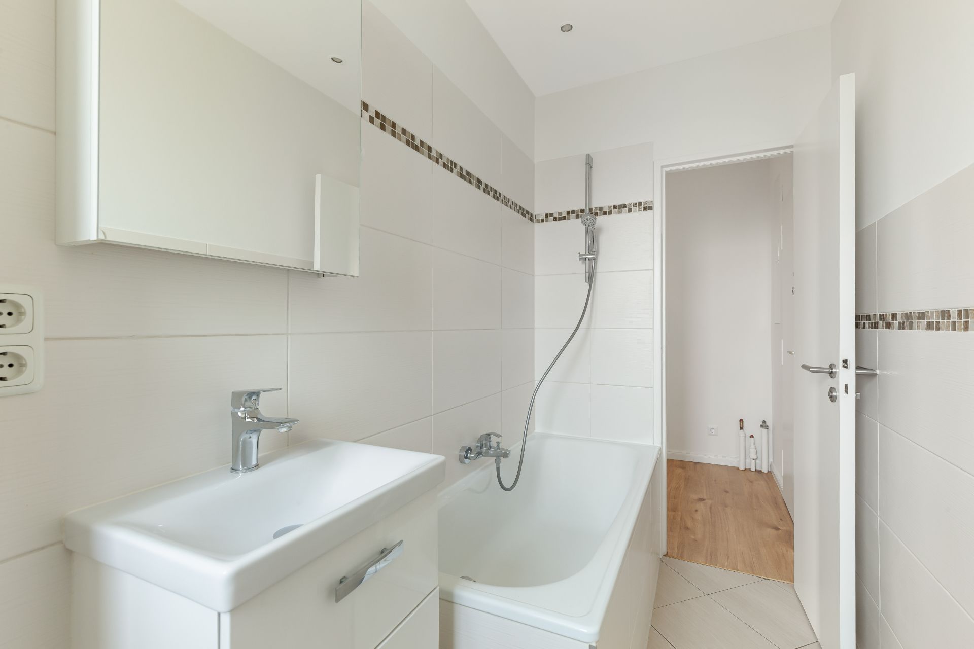 Modernes Badezimmer mit Badewanne, Waschbecken und Wandspiegel, weiß gefliest.