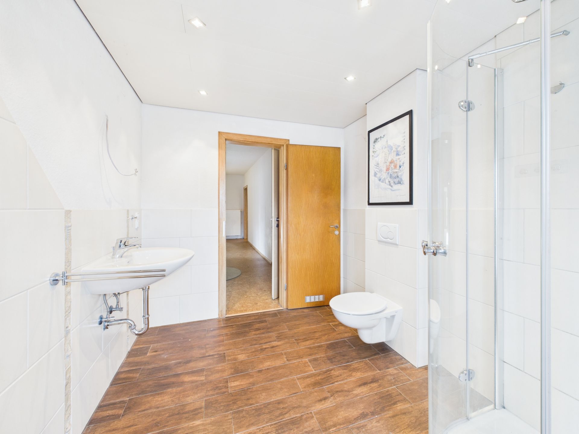 Modernes Badezimmer mit Holzoptik-Boden, Dusche, Waschbecken und Wandtoilette.