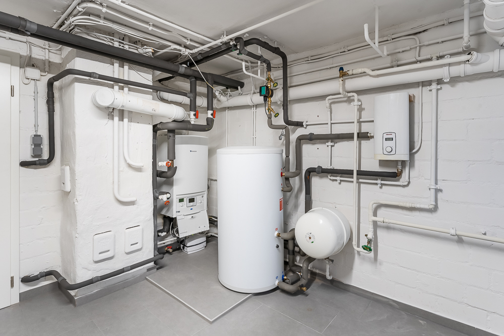 Technikraum mit Heizungsanlage, Wasserspeicher und vielen Rohrleitungen.