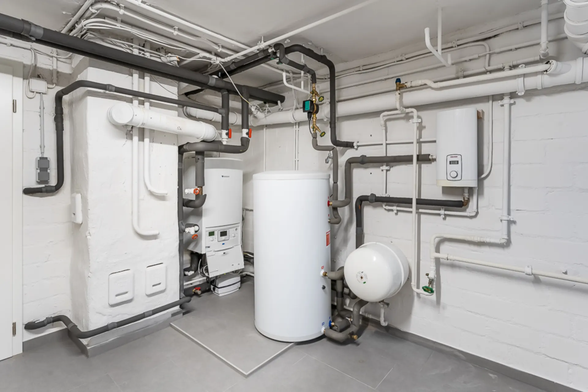 Technikraum mit Heizungsanlage, Wasserspeicher und vielen Rohrleitungen.