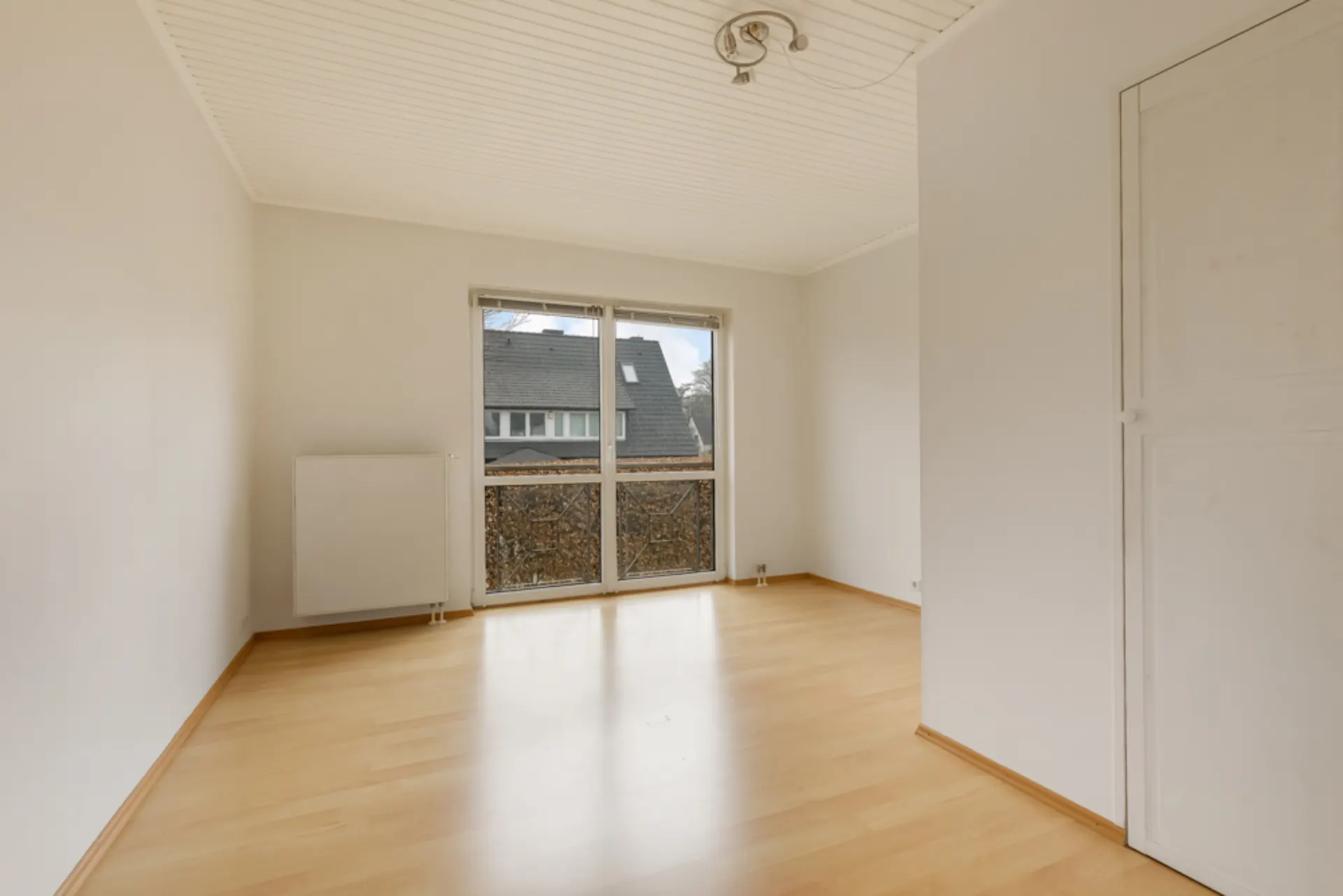Heller, leerer Raum mit Holzfußboden, großem Fenster und weißer Decke.