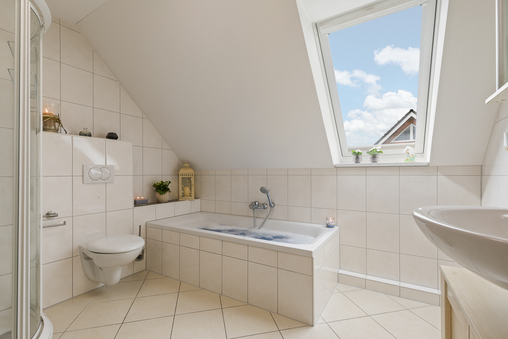 Helles Badezimmer mit Badewanne, WC, Waschbecken und großem Fenster unter Dachschräge.