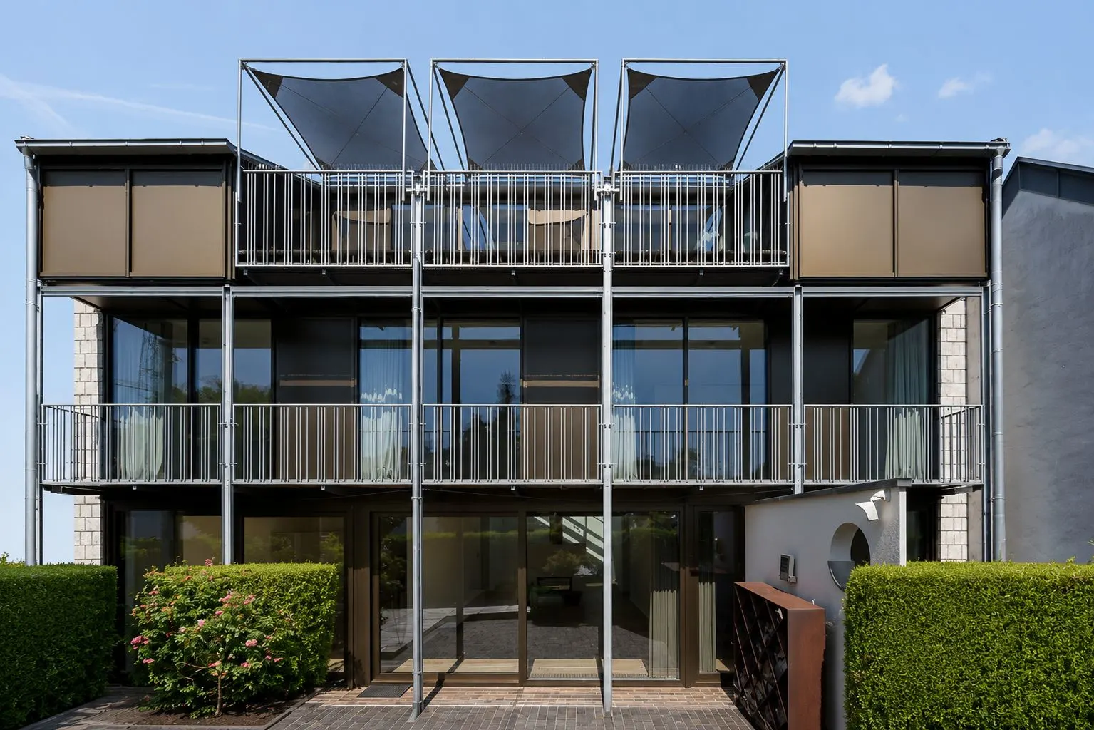 Moderne Fassade eines dreistöckigen Wohnhauses mit Balkonen und großen Glasflächen.