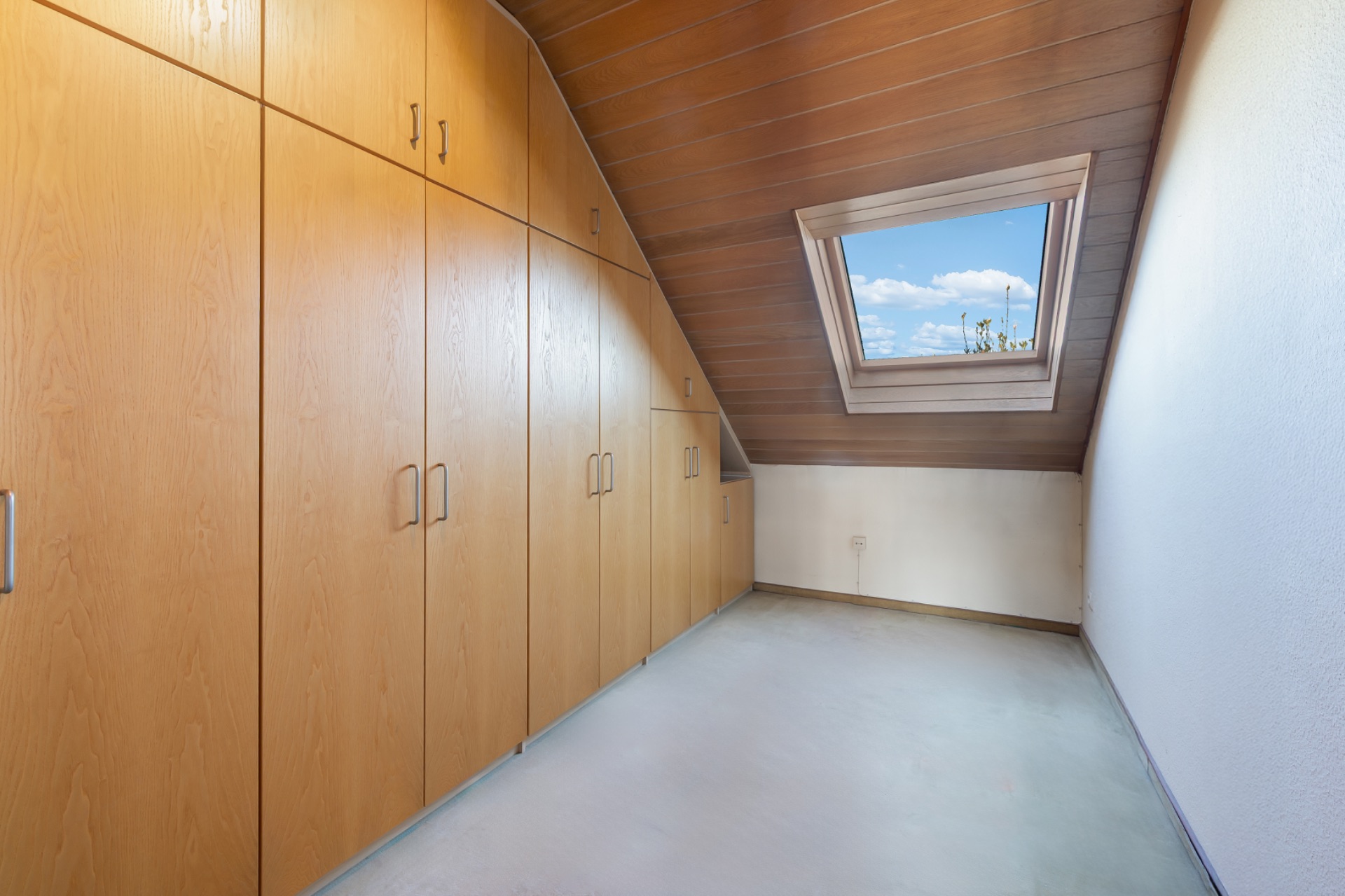 Raum mit Einbauschränken aus Holz und Dachfenster unter einer Holzdecke.