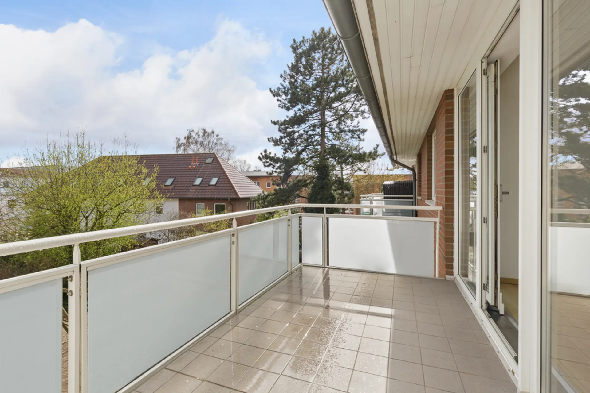 Balkon mit hellen Fliesen und weißem Geländer, Blick auf Bäume und Nachbarhäuser.