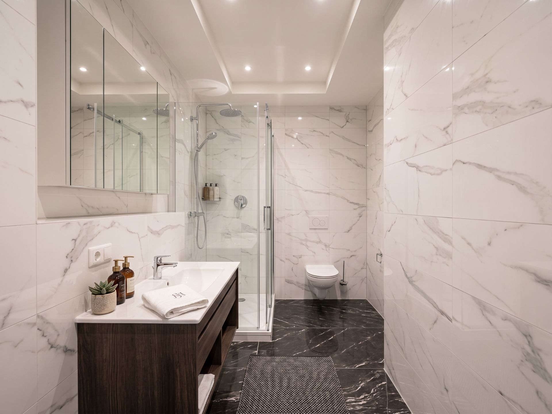Modernes Badezimmer mit Marmorfliesen, Dusche, Waschbecken und WC.