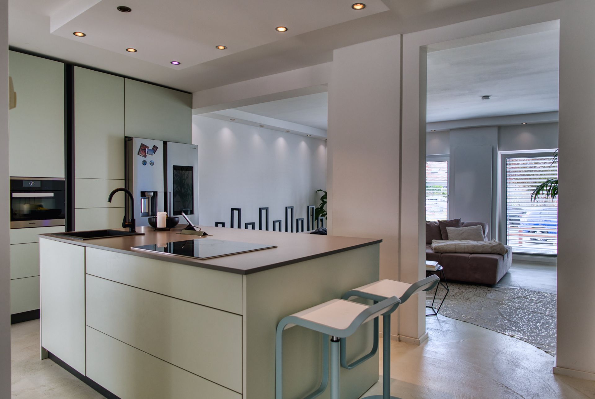 Moderne offene Küche mit Kochinsel, Hockern und angrenzendem Wohnzimmer mit Sofa.