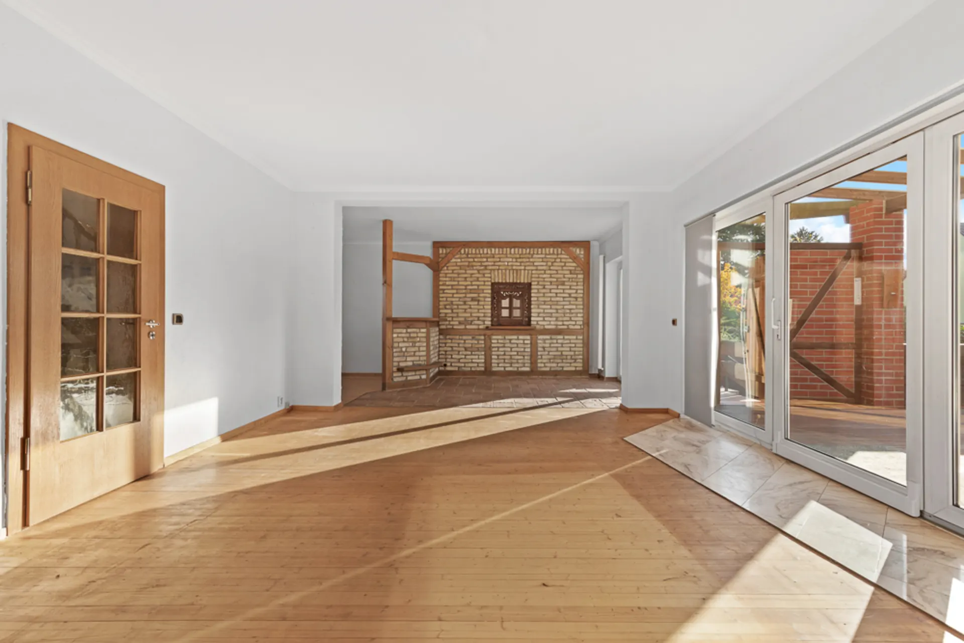 Heller Wohnraum mit Holzboden, Glastür, offener Wand und großen Fenstern zum Garten.