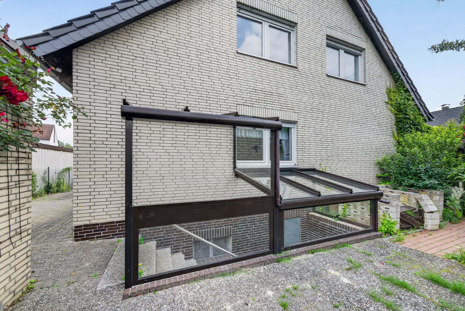 Außenansicht eines Hauses mit überdachtem Kellereingang und zwei Fenstern im Obergeschoss.