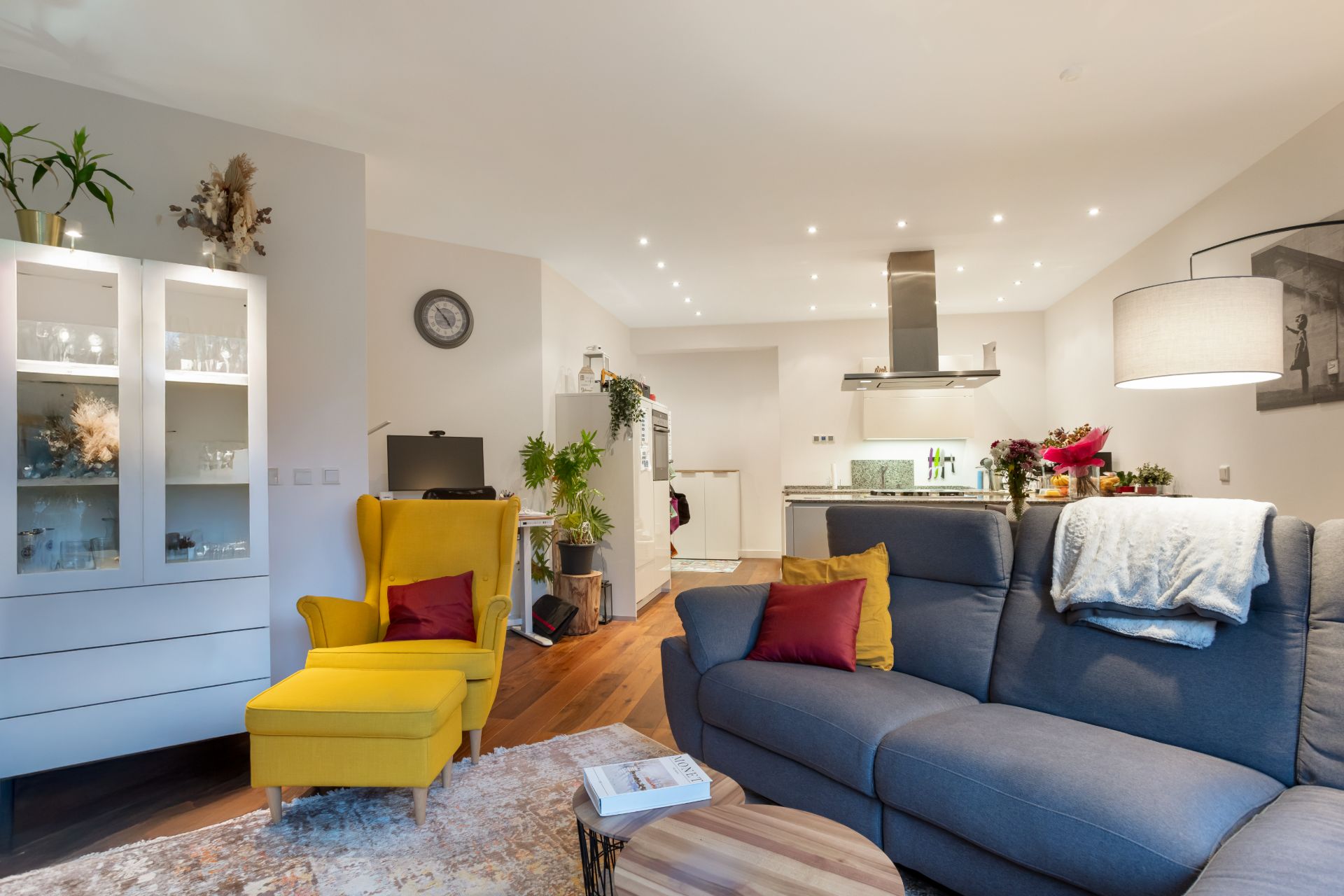 Modernes Wohnzimmer mit gelbem Sessel, grauem Sofa und offener Küche im Hintergrund.