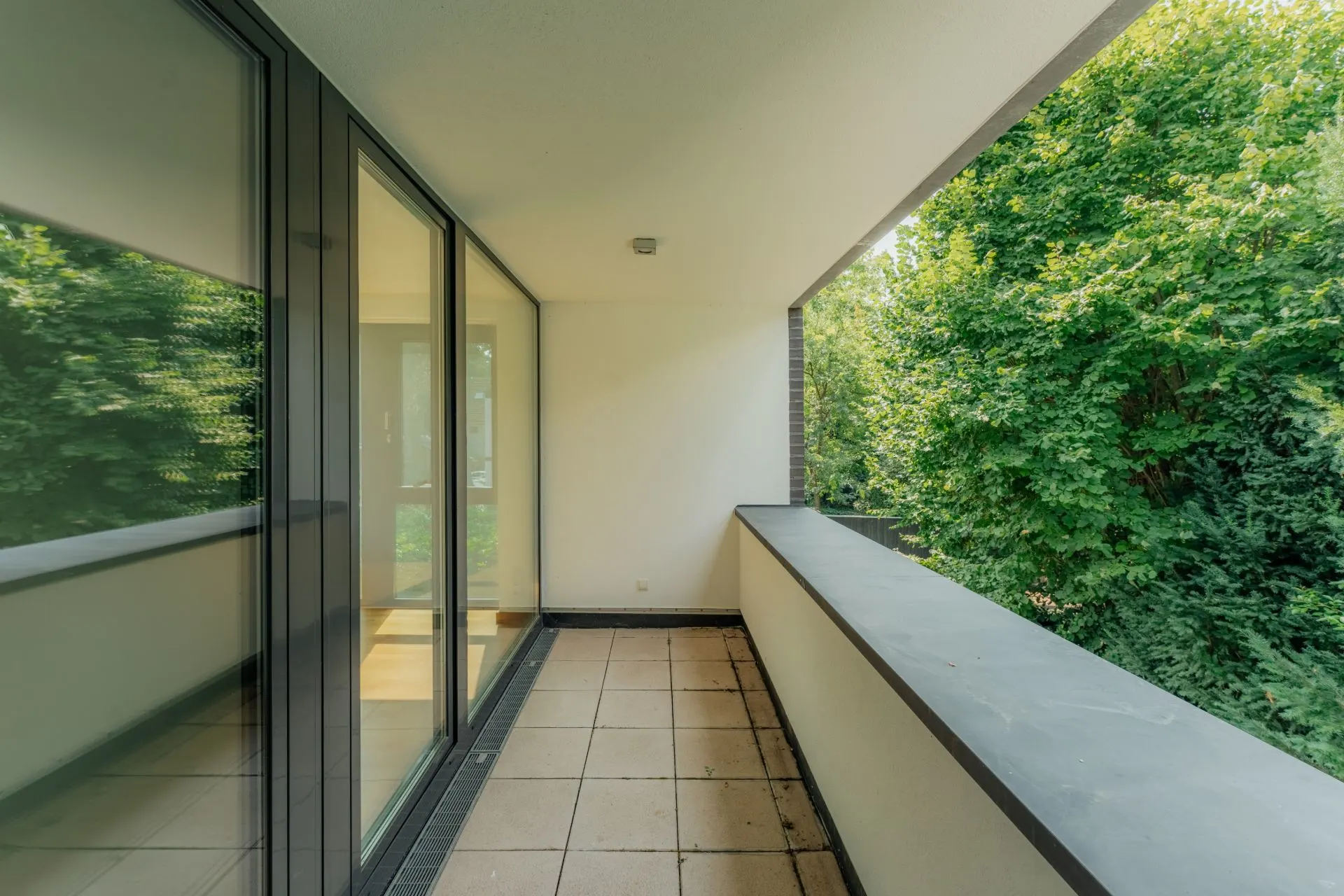 Überdachter Balkon mit Fliesenboden und Blick auf grüne Bäume.