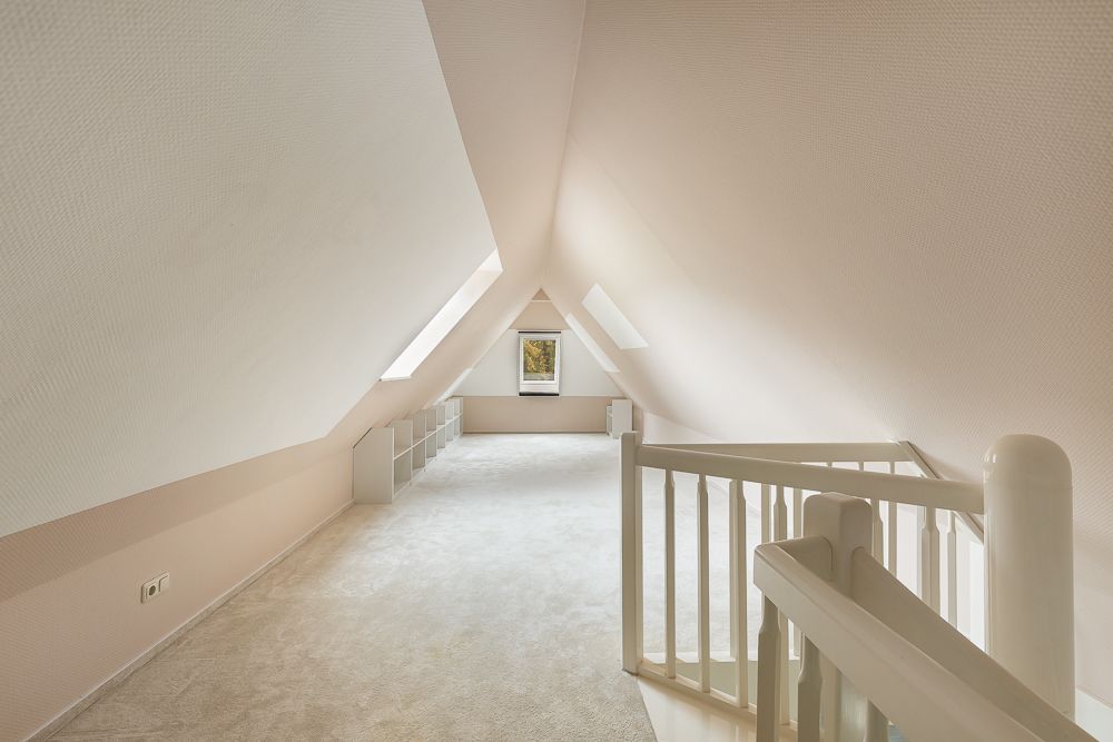Helles Dachgeschosszimmer mit Teppichboden, Fenster und weißem Treppengeländer.