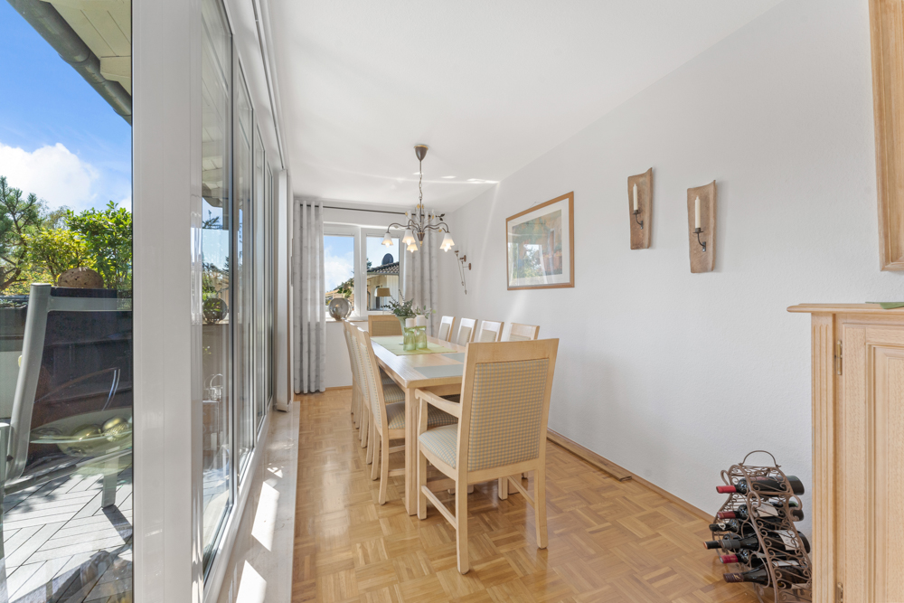 Heller Essbereich mit Holzfußboden, großem Tisch und acht Stühlen an einem Fenster mit Blick nach draußen.