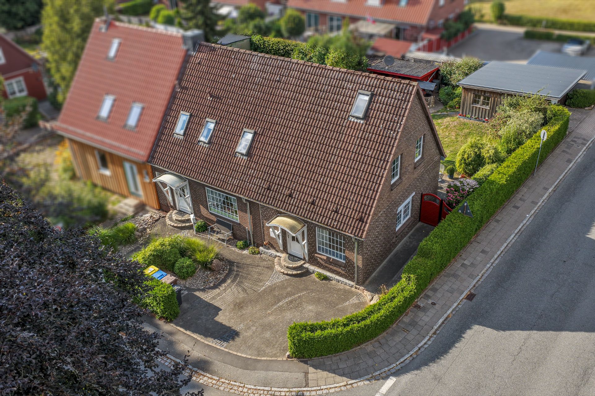 Zweistöckiges Wohnhaus mit rotem Dach, Vorgarten und zwei Hauseingängen an einer ruhigen Straße.