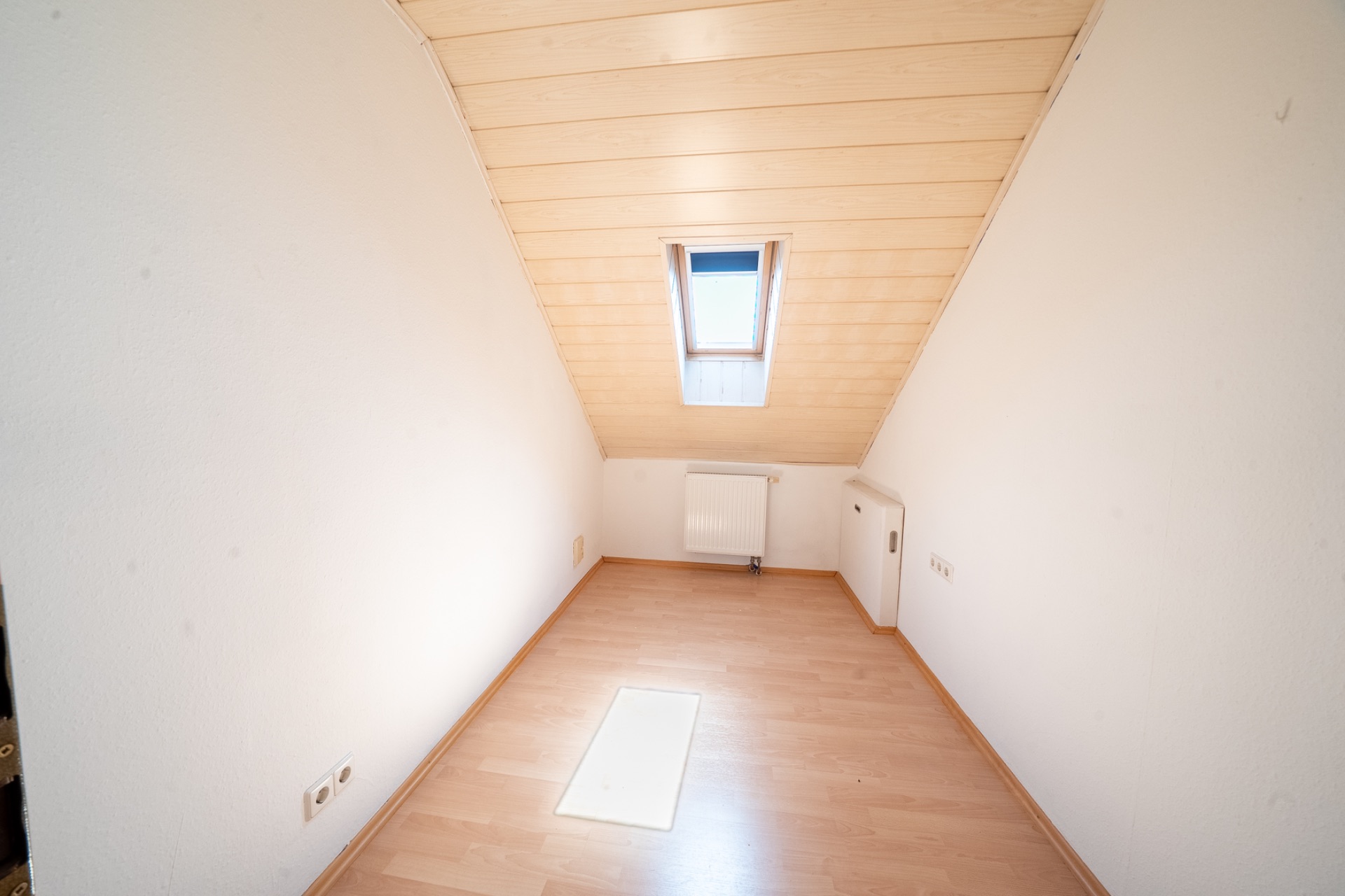 Kleiner Dachraum mit Holzdecke, Laminatboden, Dachfenster und Heizkörper.