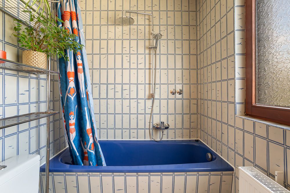 Badezimmer mit blauer Badewanne, Duschvorhang und gefliesten Wänden.