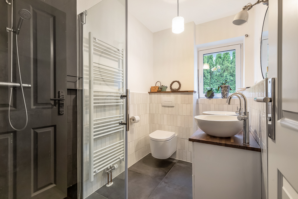 Modernes Badezimmer mit Dusche, Waschbecken, WC und Fenster mit Blick ins Grüne.