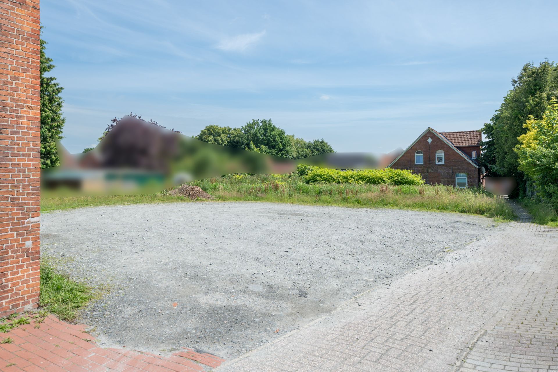 Leerer, geschotterter Platz neben einem Wohnhaus mit grüner Umgebung.