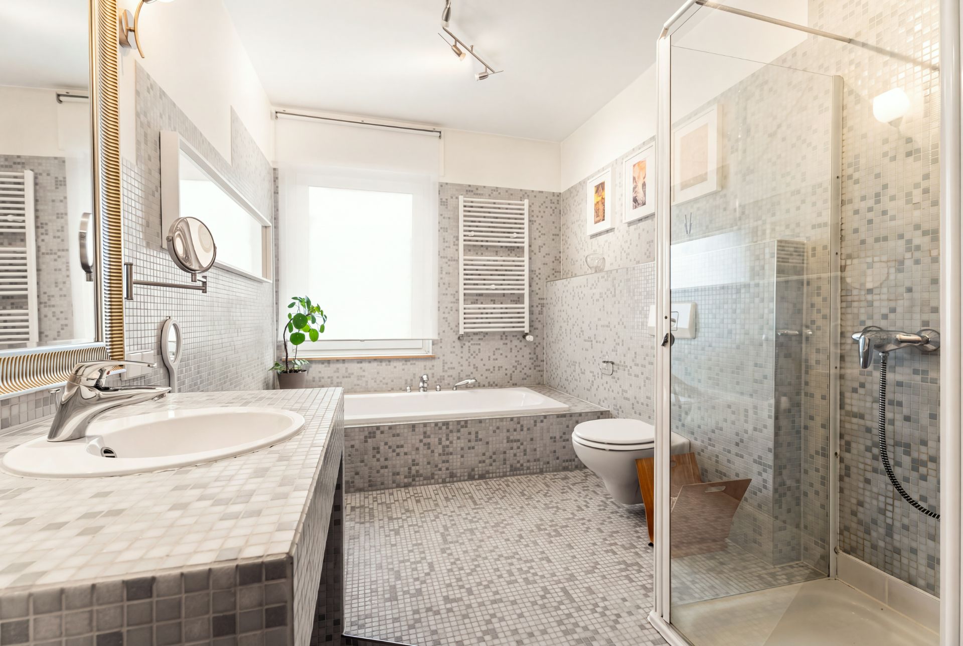 Helles Badezimmer mit Waschbecken, Badewanne, Toilette und Glasdusche, alles mit Mosaikfliesen.