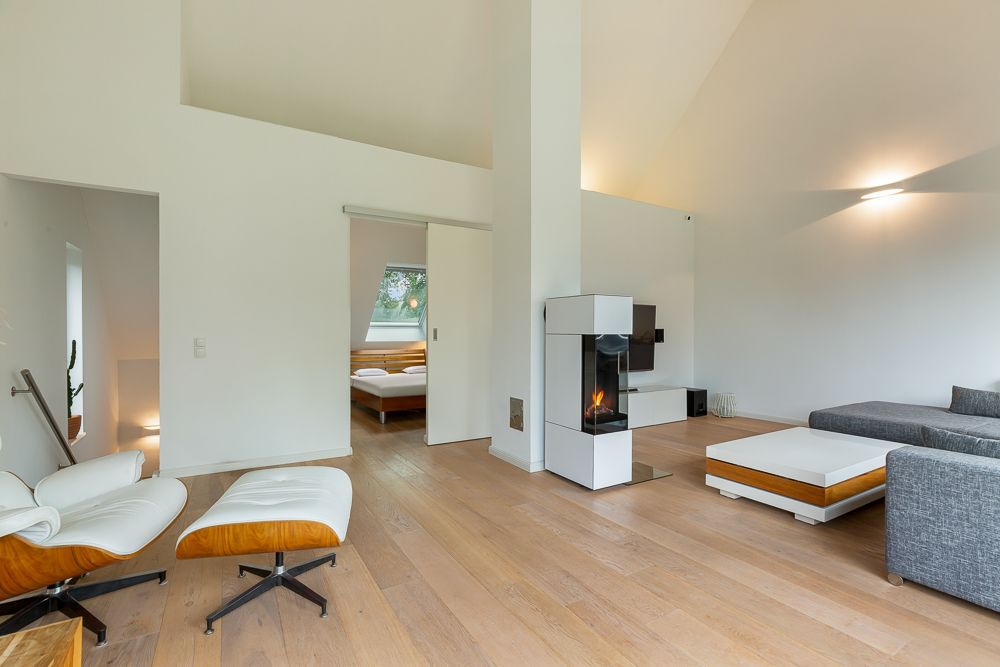 Modernes Wohnzimmer mit Kamin, grauem Sofa, Sessel und Blick ins Schlafzimmer.