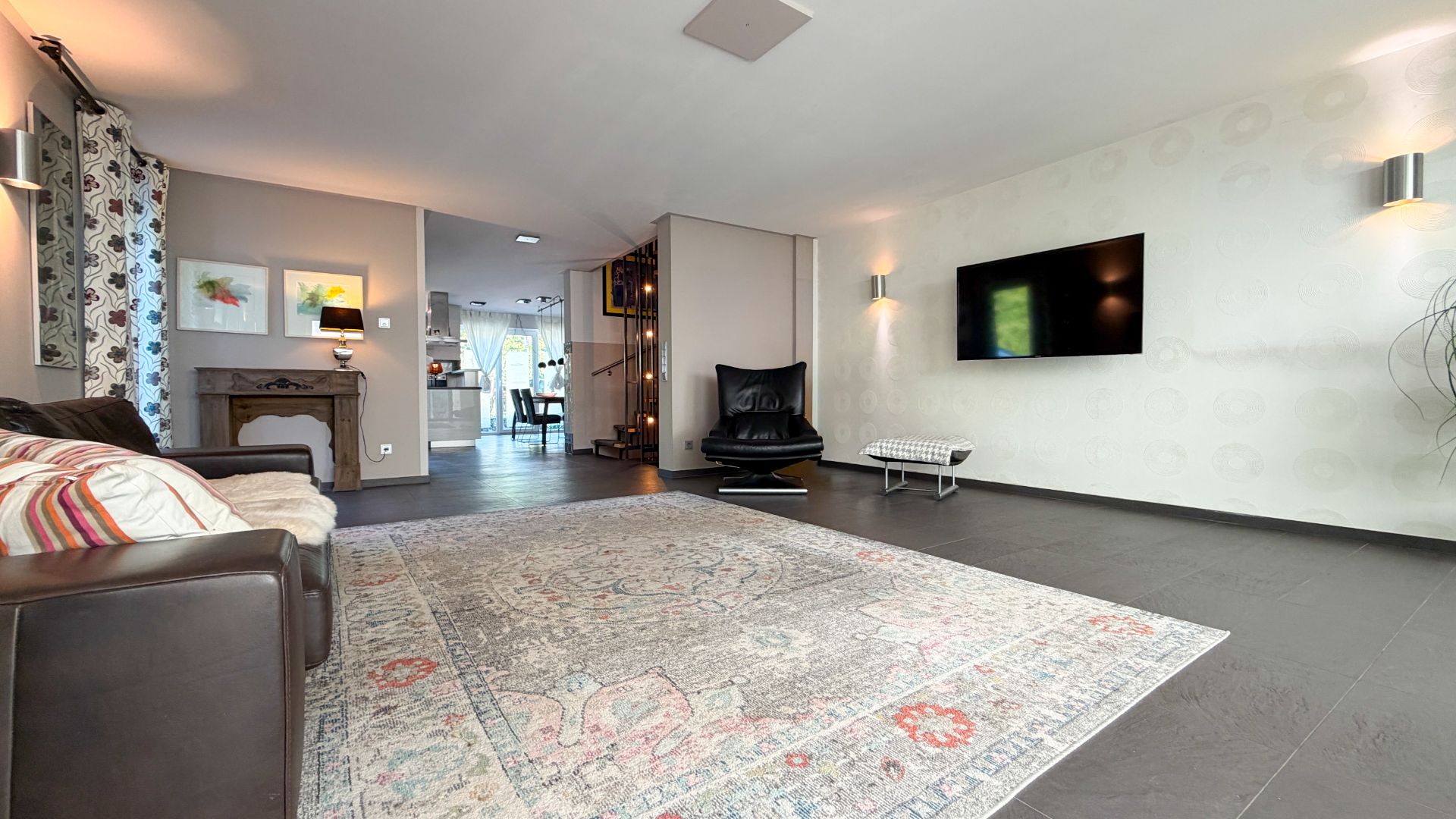 Modernes Wohnzimmer mit großem Teppich, Sofa, Sessel, Wand-TV und dekorativen Bildern.