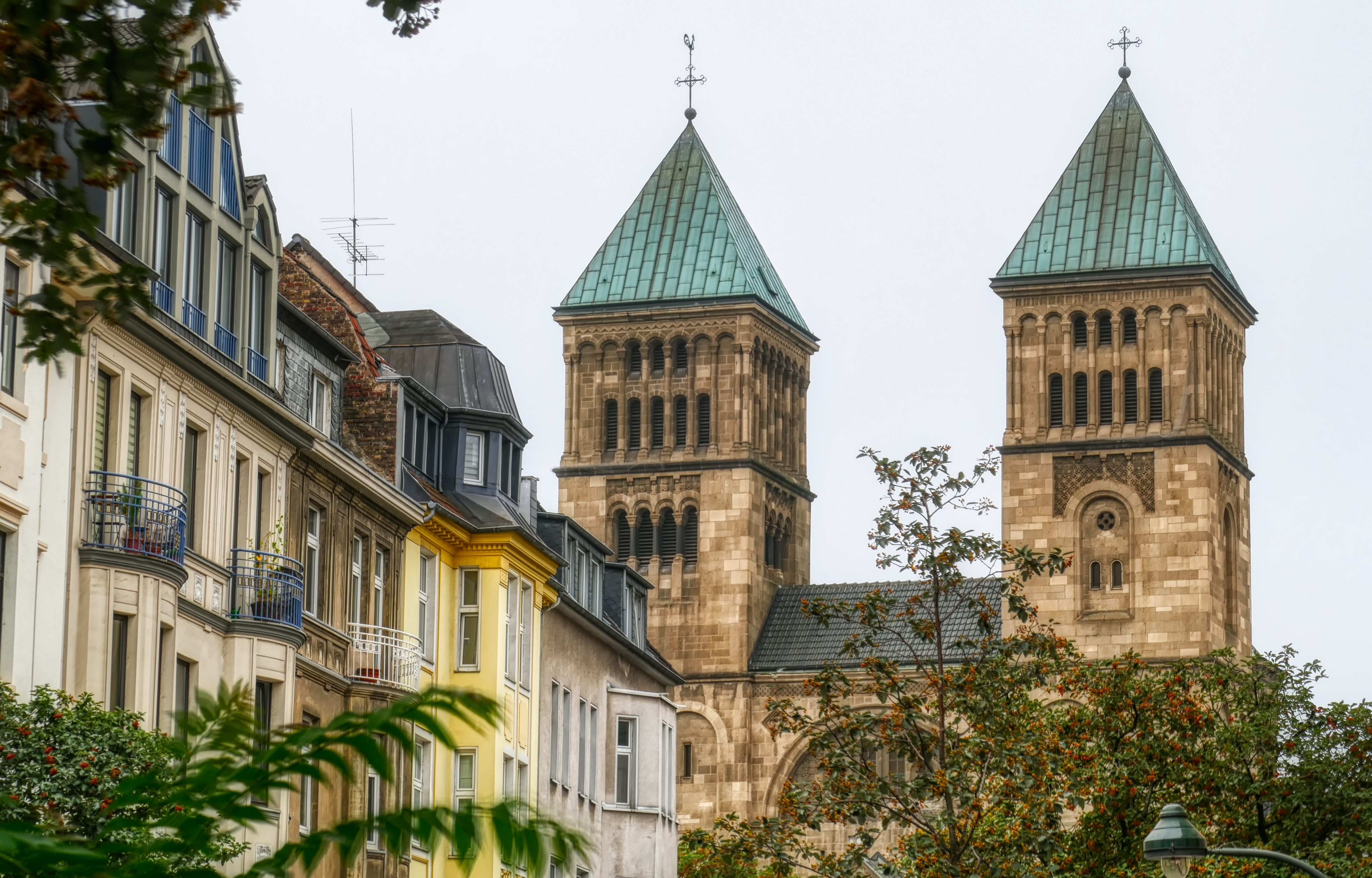 Backsteingebäude mit hohem Turm und großen Fenstern, umgeben von Bäumen und Hecken.