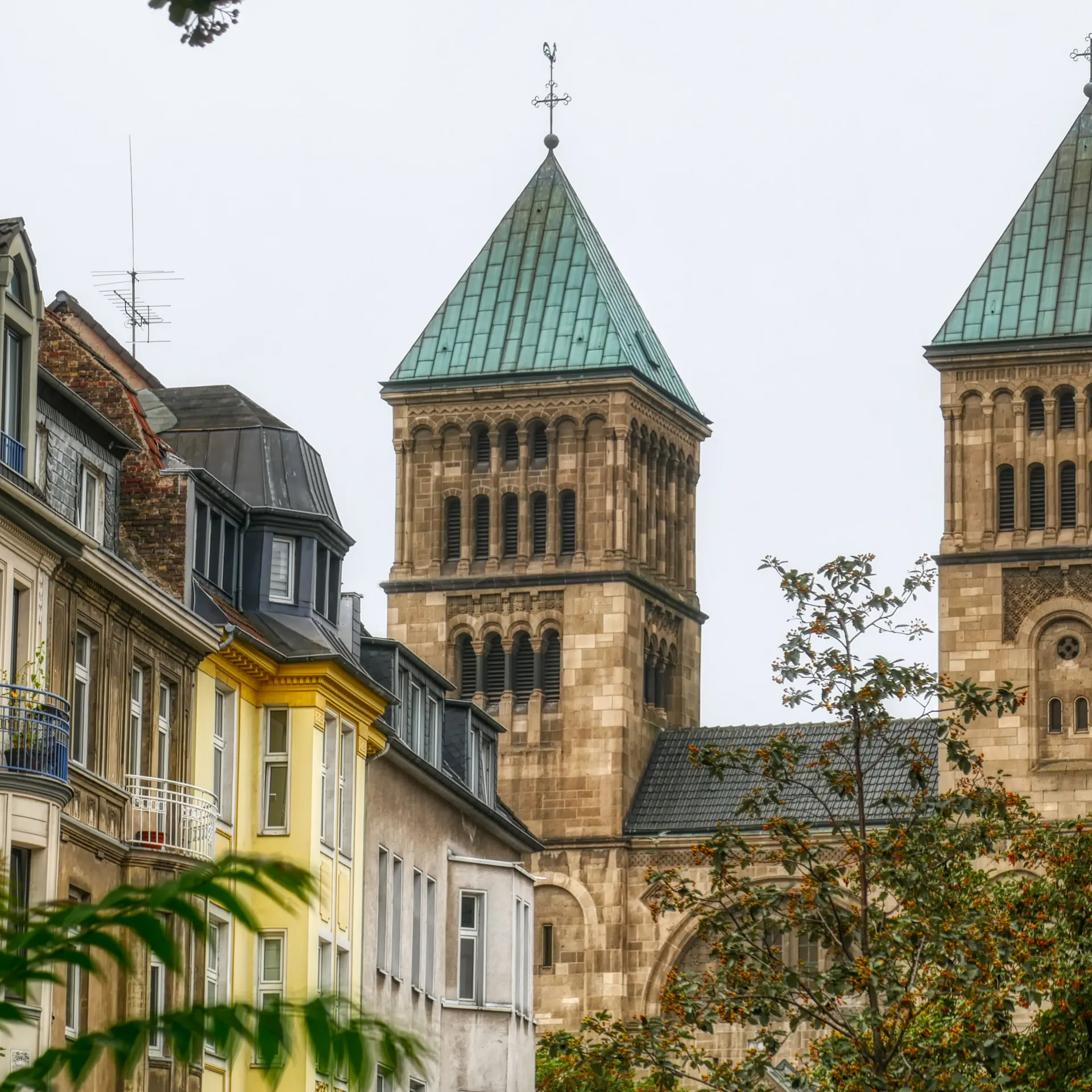 Backsteingebäude mit hohem Turm und großen Fenstern, umgeben von Bäumen und Hecken.