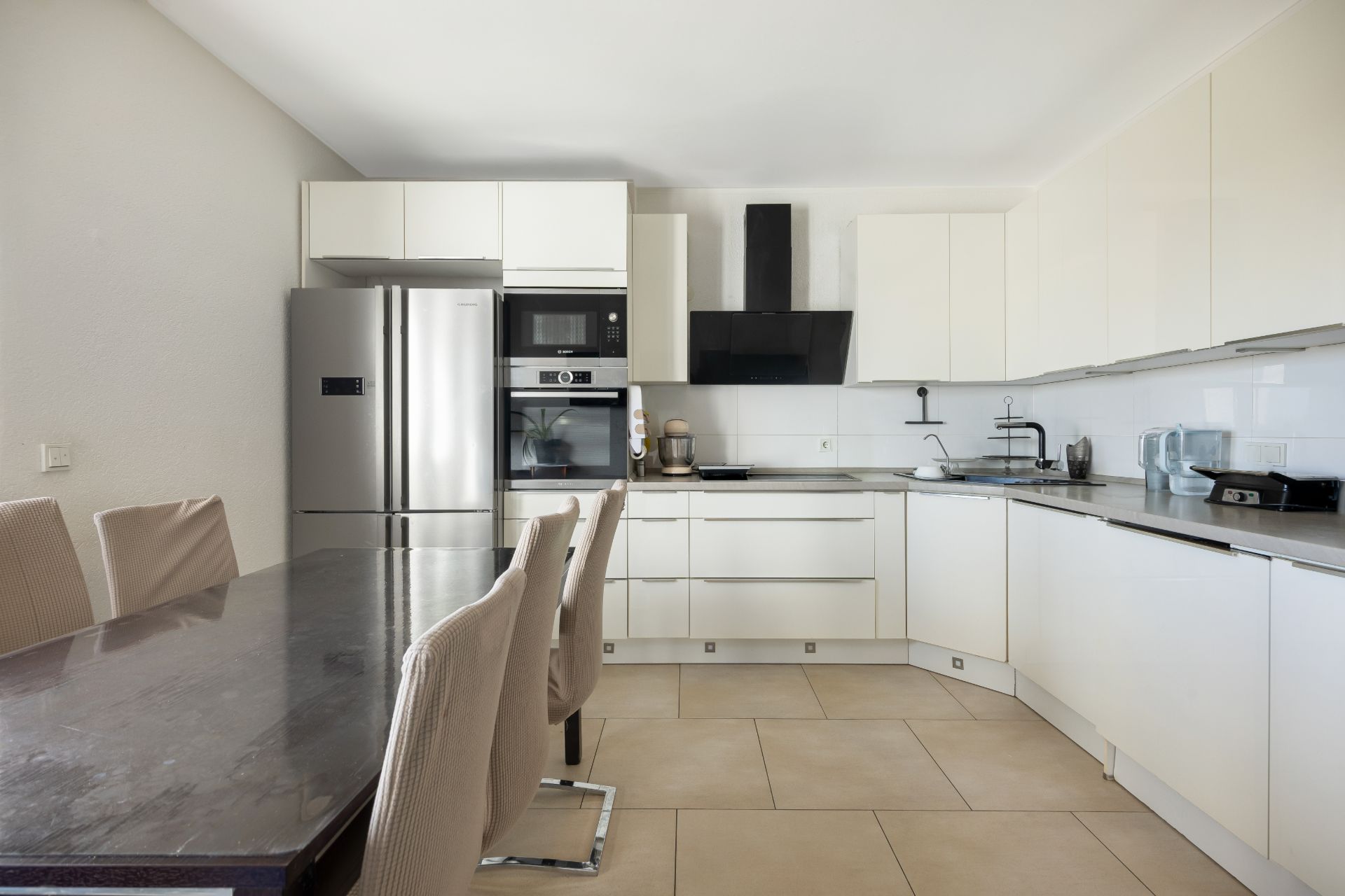 Moderne Einbauküche mit Esstisch, Stühlen, Kühlschrank und weißen Schränken.