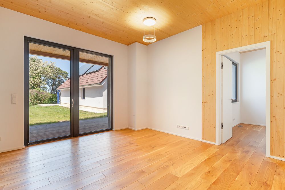 Heller Raum mit Holzboden, großen Fenstern zur Terrasse und Holzdecke.