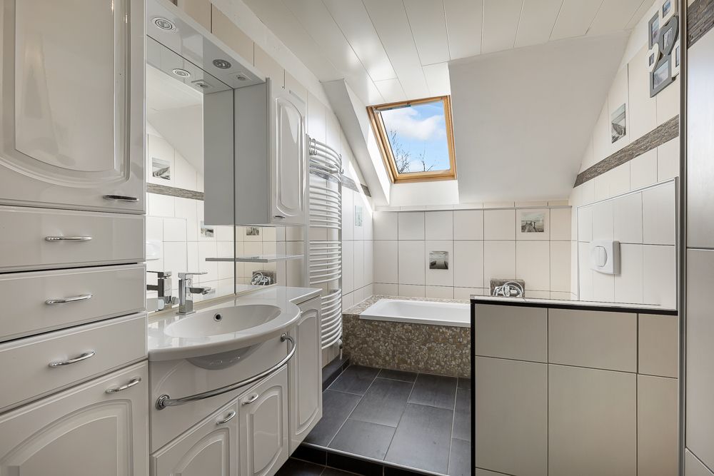 Modernes Badezimmer mit Dachfenster, Badewanne, Waschbecken und weißen Fliesen.
