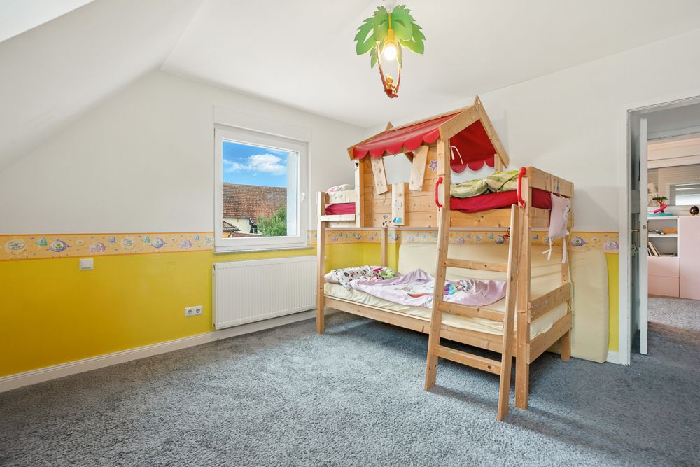 Kinderzimmer mit Etagenbett aus Holz, Fenster und bunter Wandgestaltung.