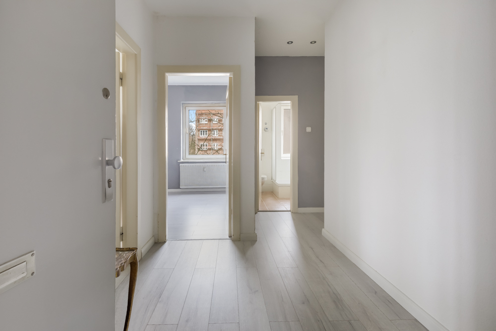 Heller Flur mit Blick in zwei Zimmer, eines mit Fenster und Heizung, das andere mit Bad.