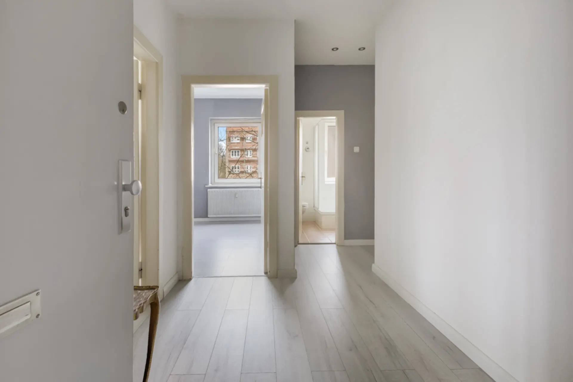 Heller Flur mit Blick in zwei Zimmer, eines mit Fenster und Heizung, das andere mit Bad.