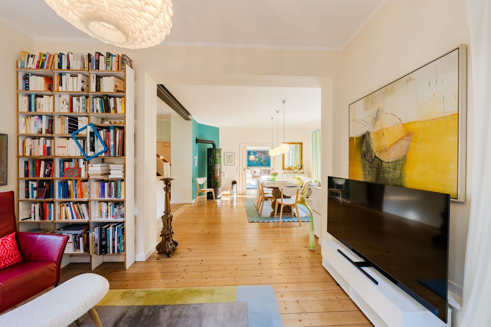 Wohnzimmer mit Bücherregal, rotem Sessel, großem Fernseher und Blick ins Esszimmer mit Holzboden.