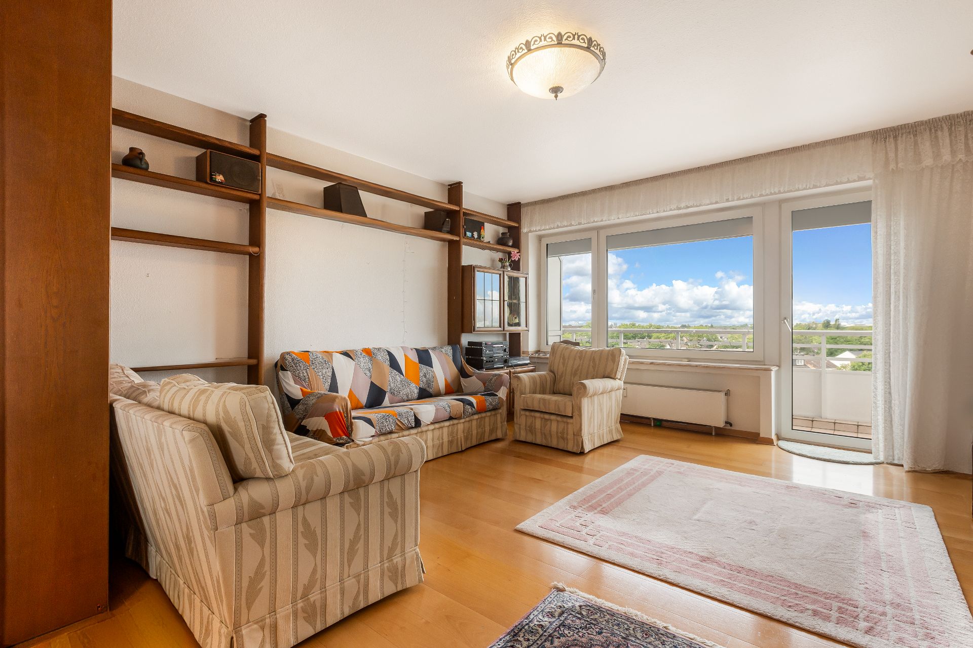 Wohnzimmer mit Sofas, Regalwand, großem Fenster und Zugang zu einem Balkon.